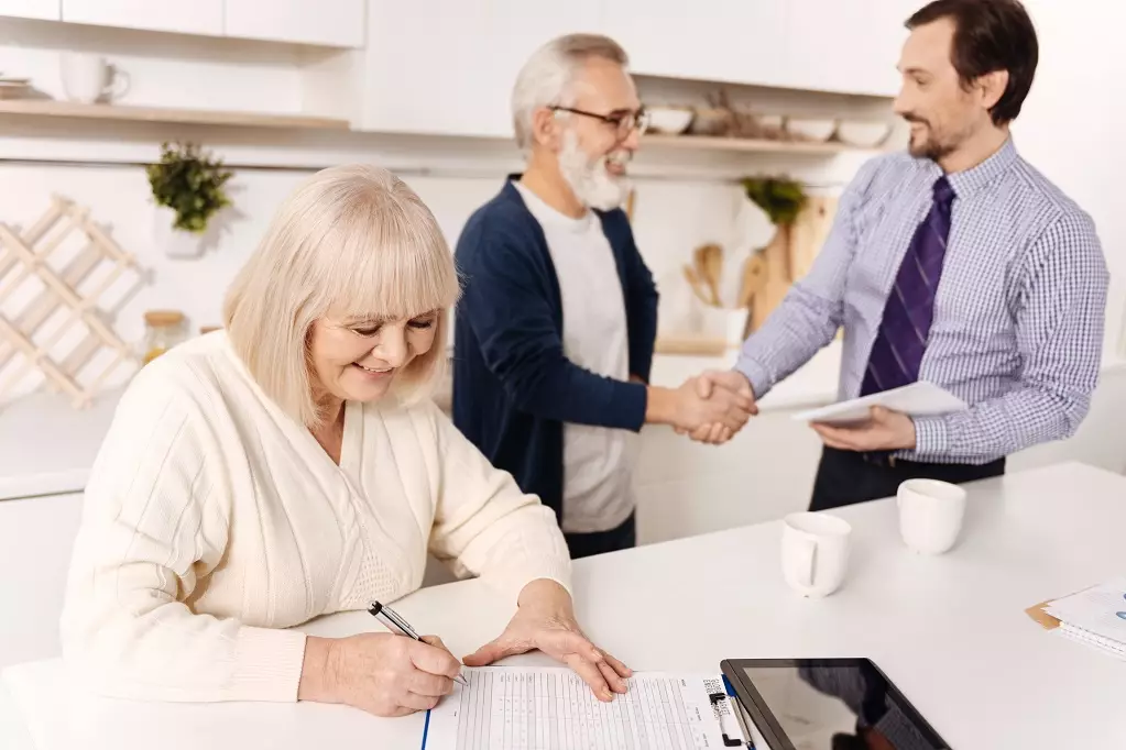 Retired woman signing contract while her husband greeting the notary